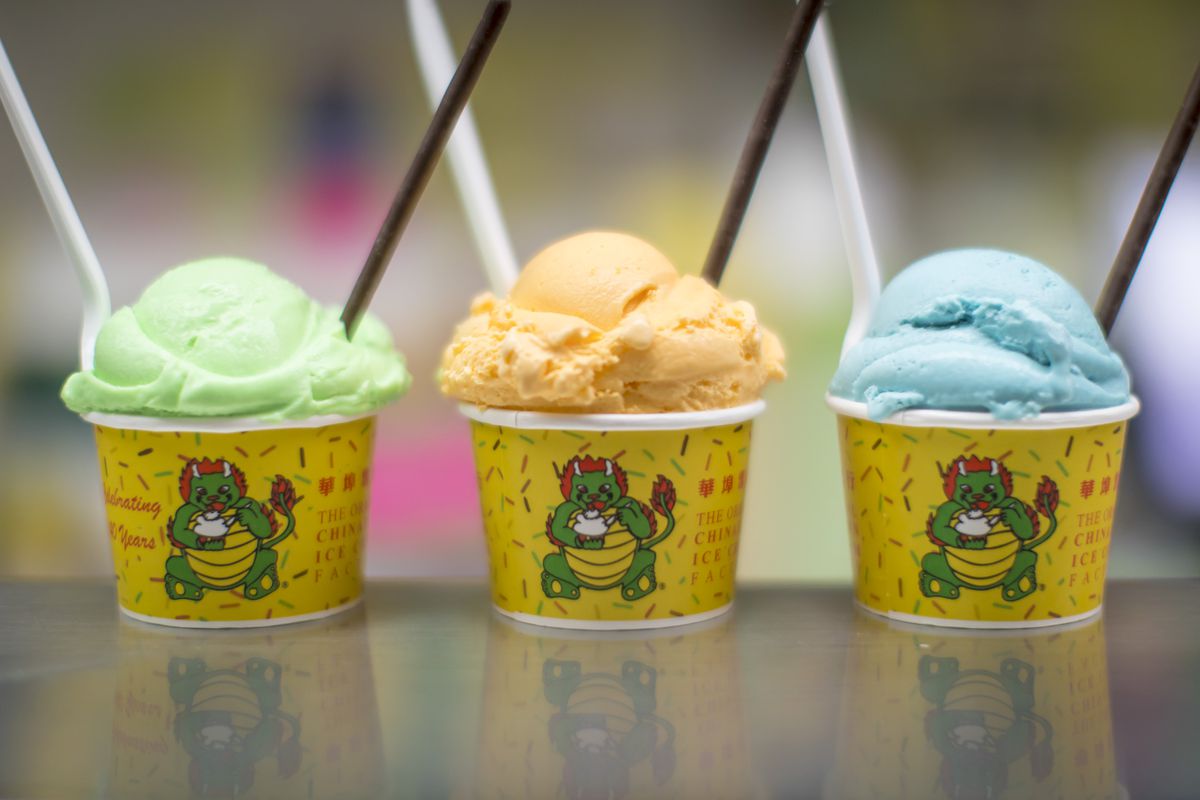 Three yellow cups with green, orange, and blue colored ice cream in them. Each of them have two spoons in them as well.