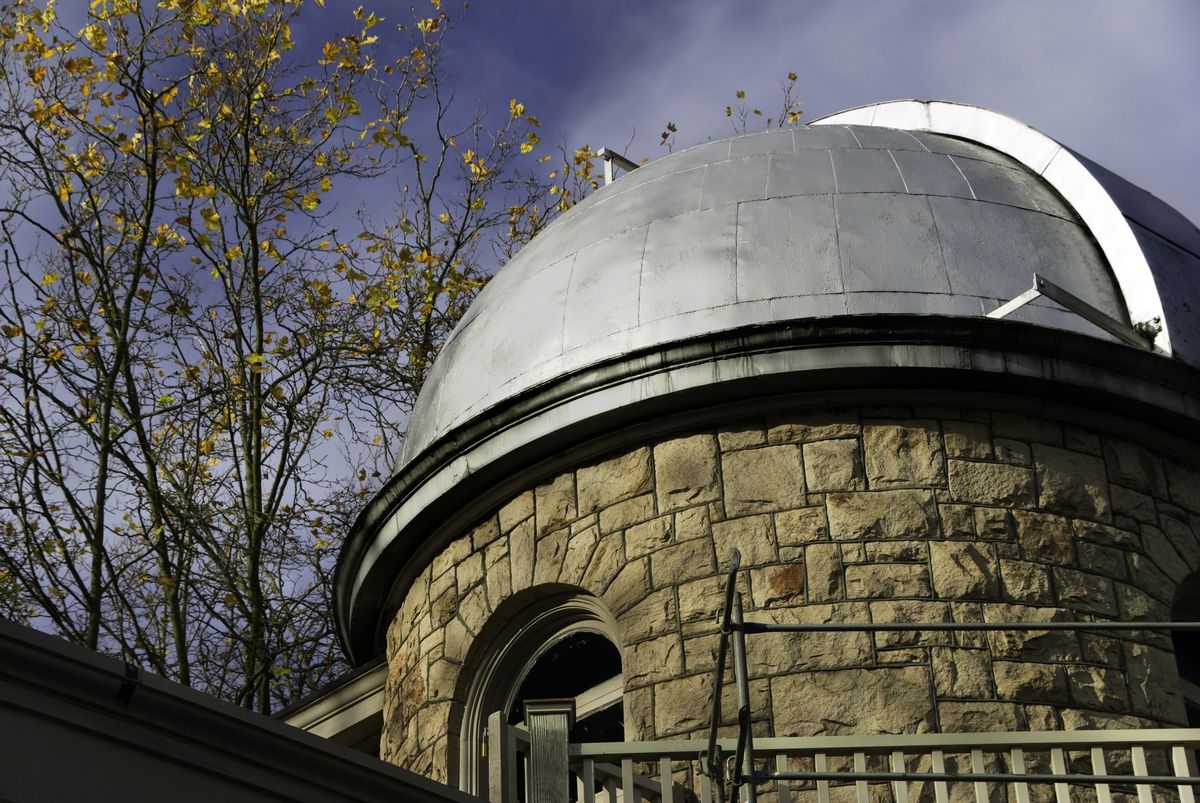 A round, stone building with a metal roof in front of a blue, slightly cloudy sky.