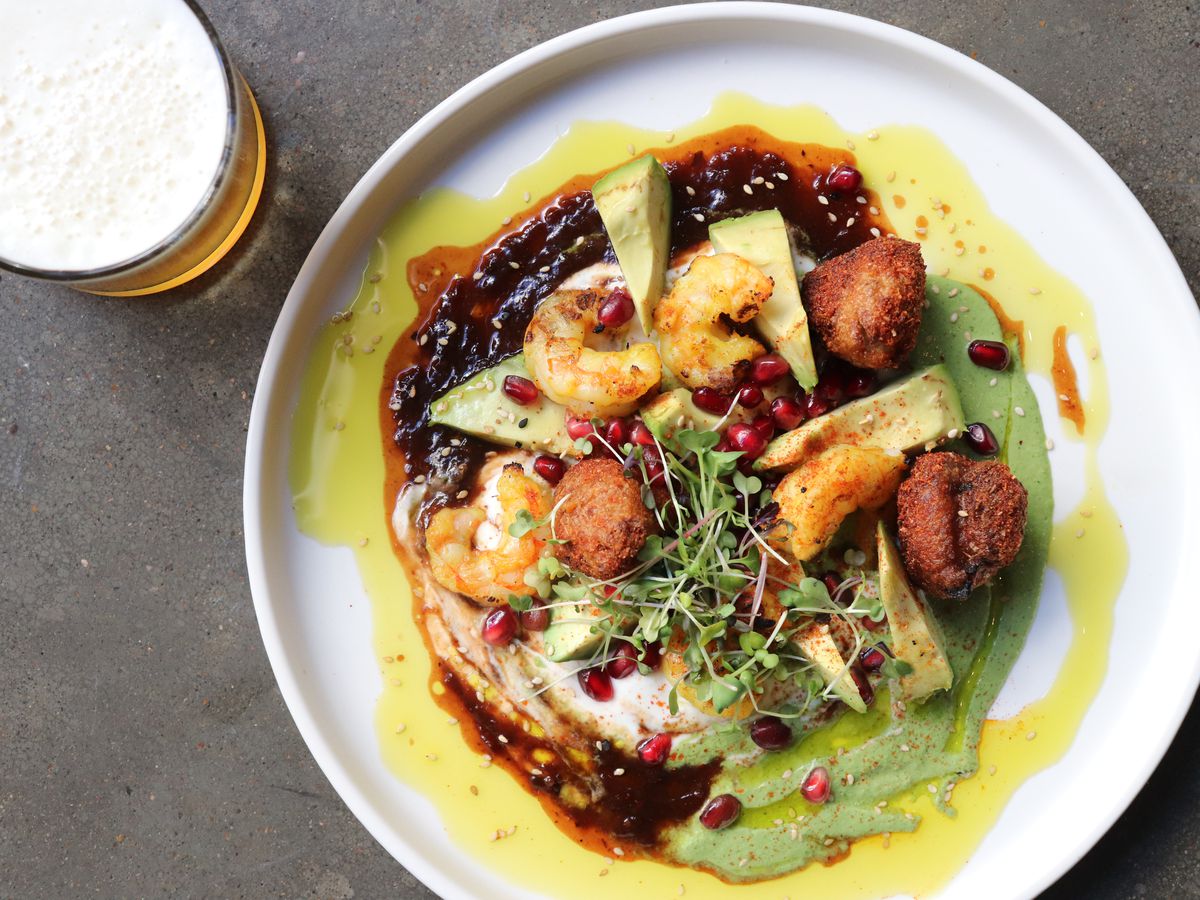 A messy plate of shrimp with a variety of chutneys, topped with pomegranate seeds.