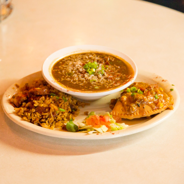 An oval plate with fried food surrounding a bow of brown gumbo. 