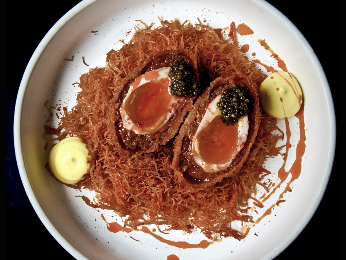 A closeup on deep red scotch eggs on a bed of noodles. 
