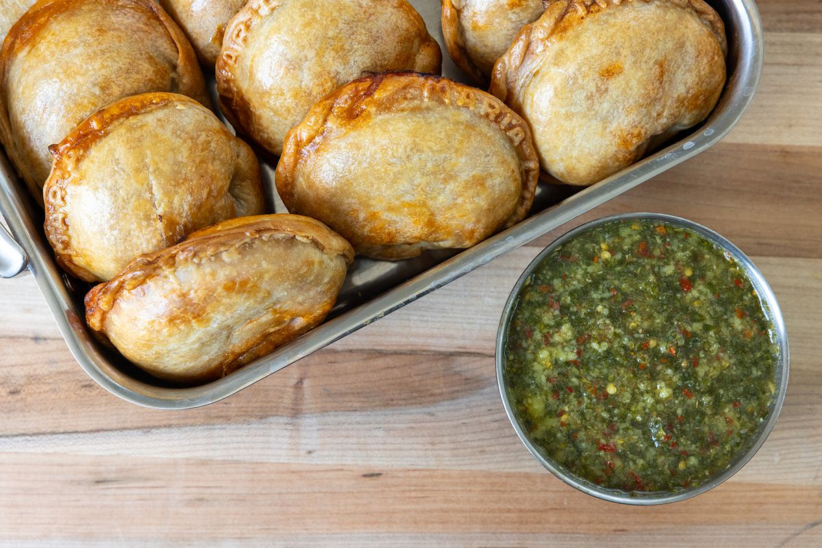 A tray of empanadas next to a dish of chimichurri sauce.