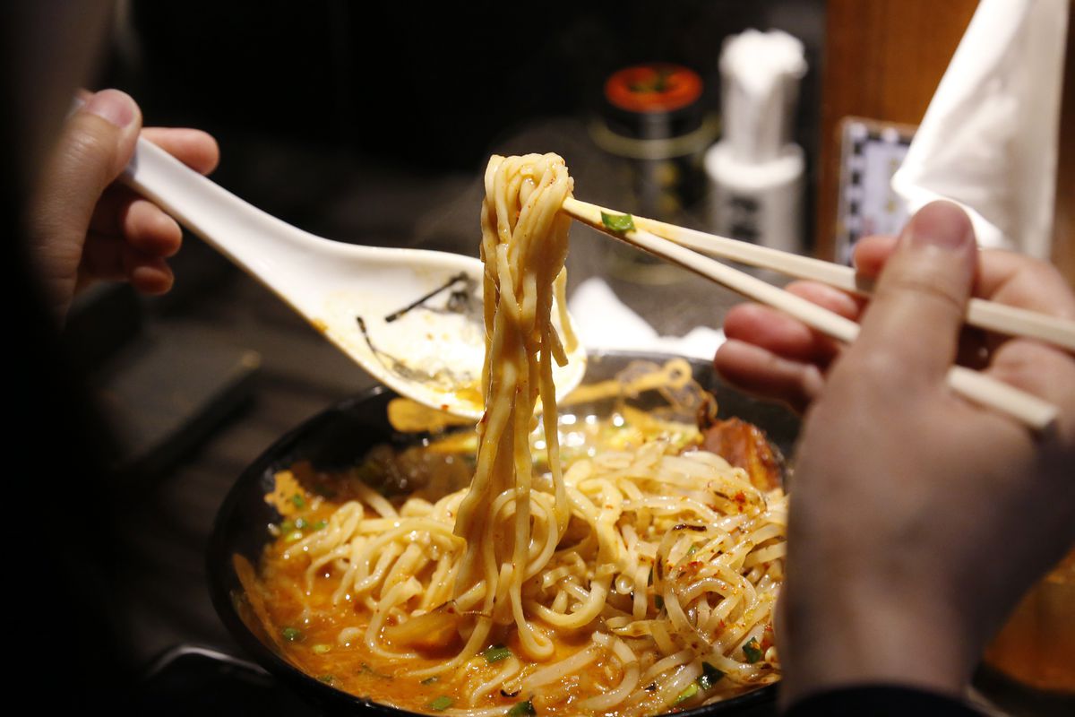 A diner lifts a bunch of ramen noodles with chopsticks. 