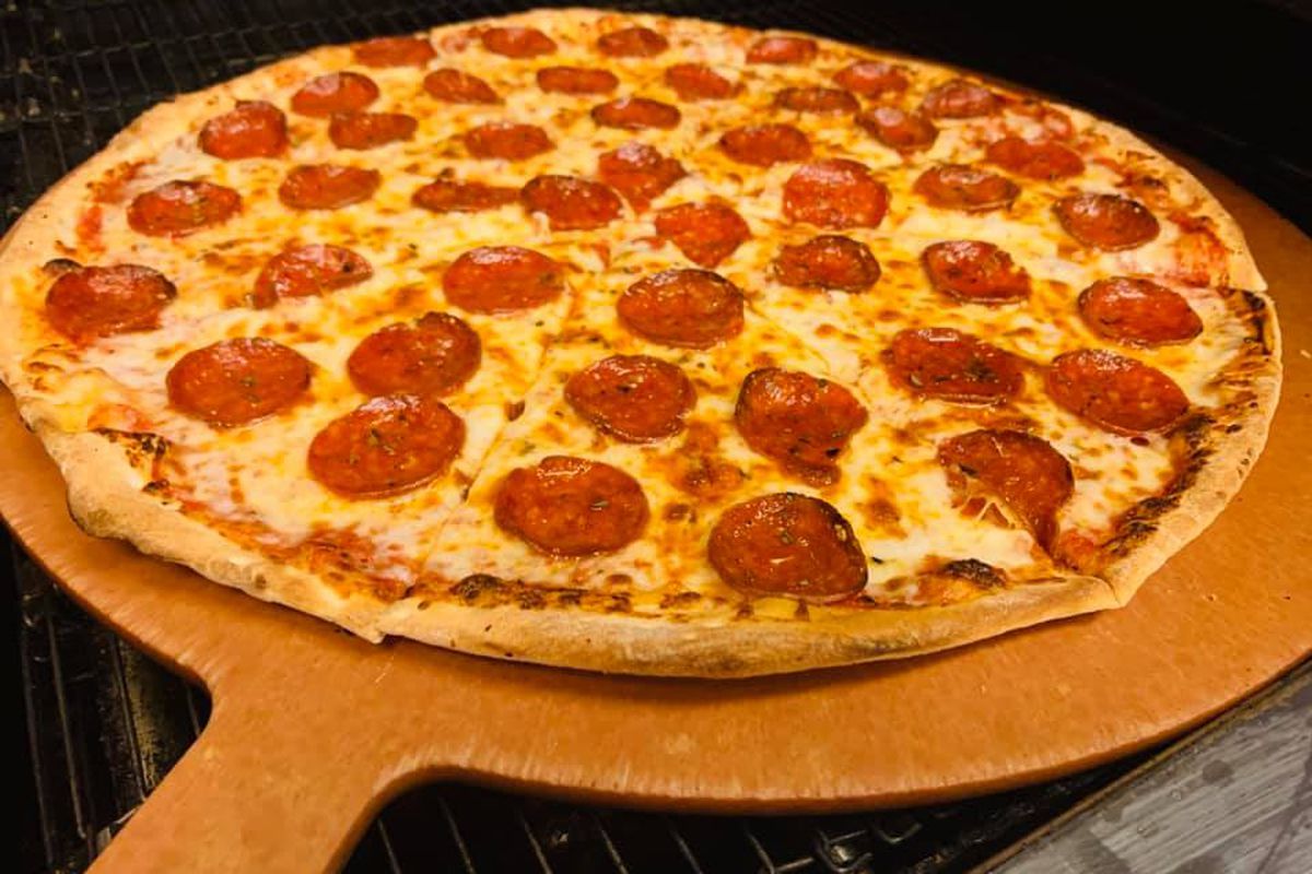 A pepperoni pizza sitting atop a pizza peel 