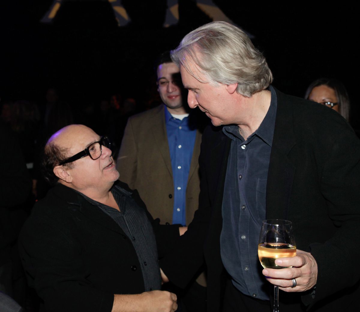 Danny Devito looks up to talk to director James Cameron, who is holding a glass of white wine at the post-Avatar party