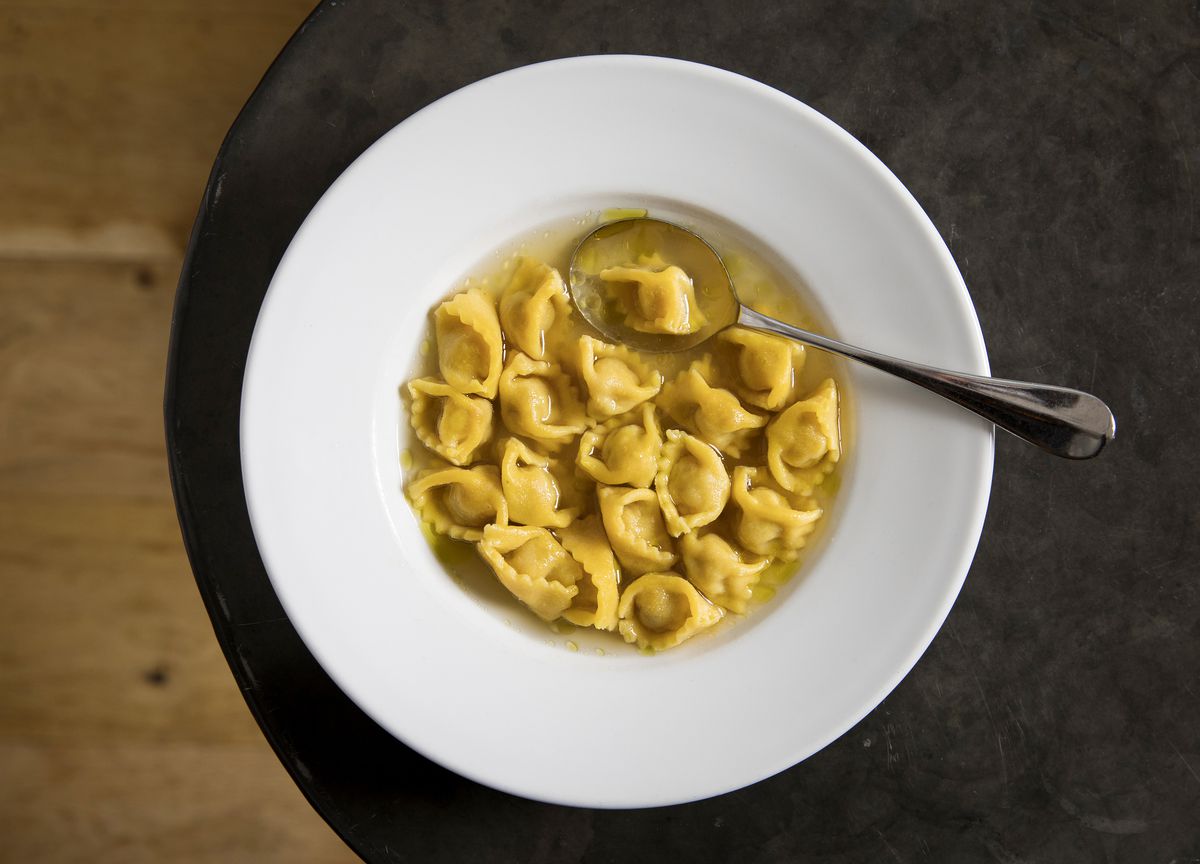 Agnolotti in broth in a white bowl on a black table