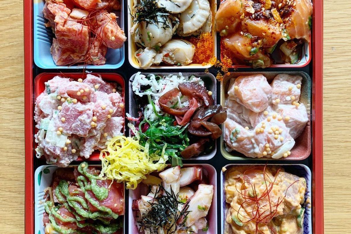 A nine-item grid bento box with white scallops, salmon with chili oil, and various other chopped raw fish covered in sauce.