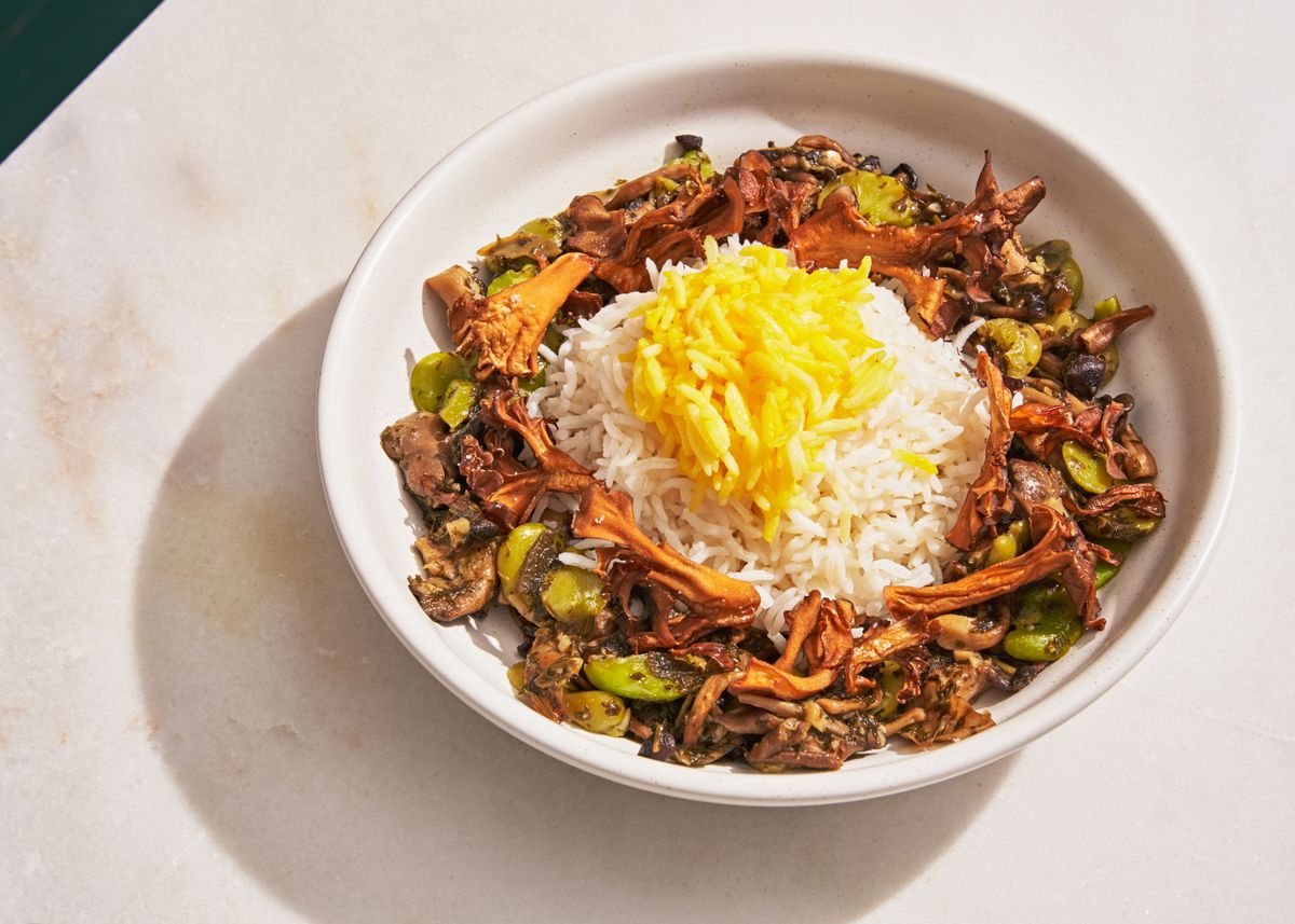 A white bowl is filled with mushrooms, fava beans, and saffron-tinged rice at the center.