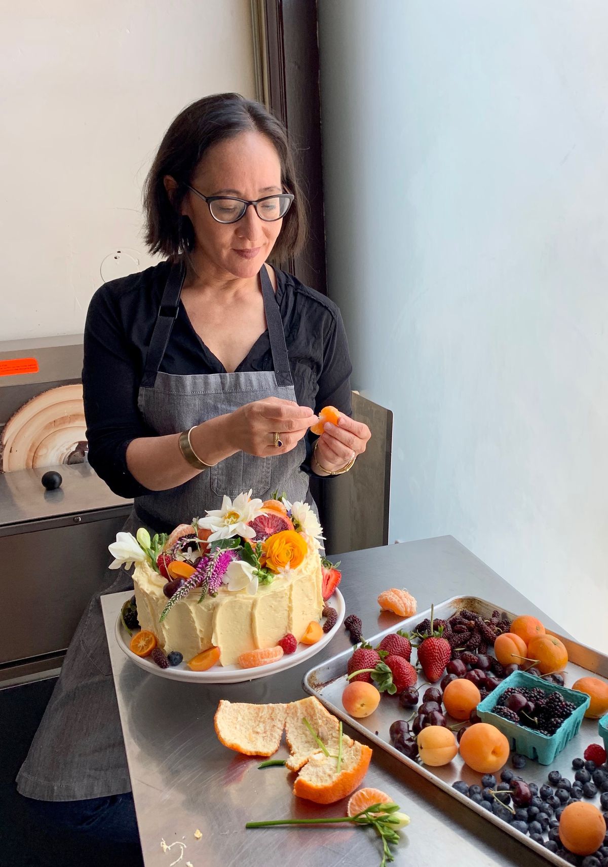 Pastry chef Valerie Gordon garnishes a frosted cake with fruit and fresh flowers.