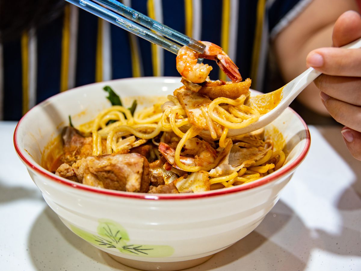 A person uses a spoon and chopsticks to eat a bowl of har meen