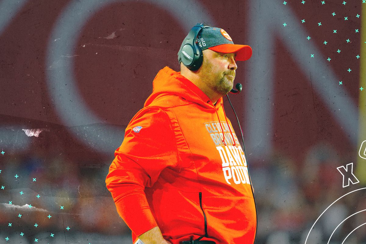 A side profile of Browns coach Freddie Kitchens, wearing a headset, with white X’s and O’s in the background