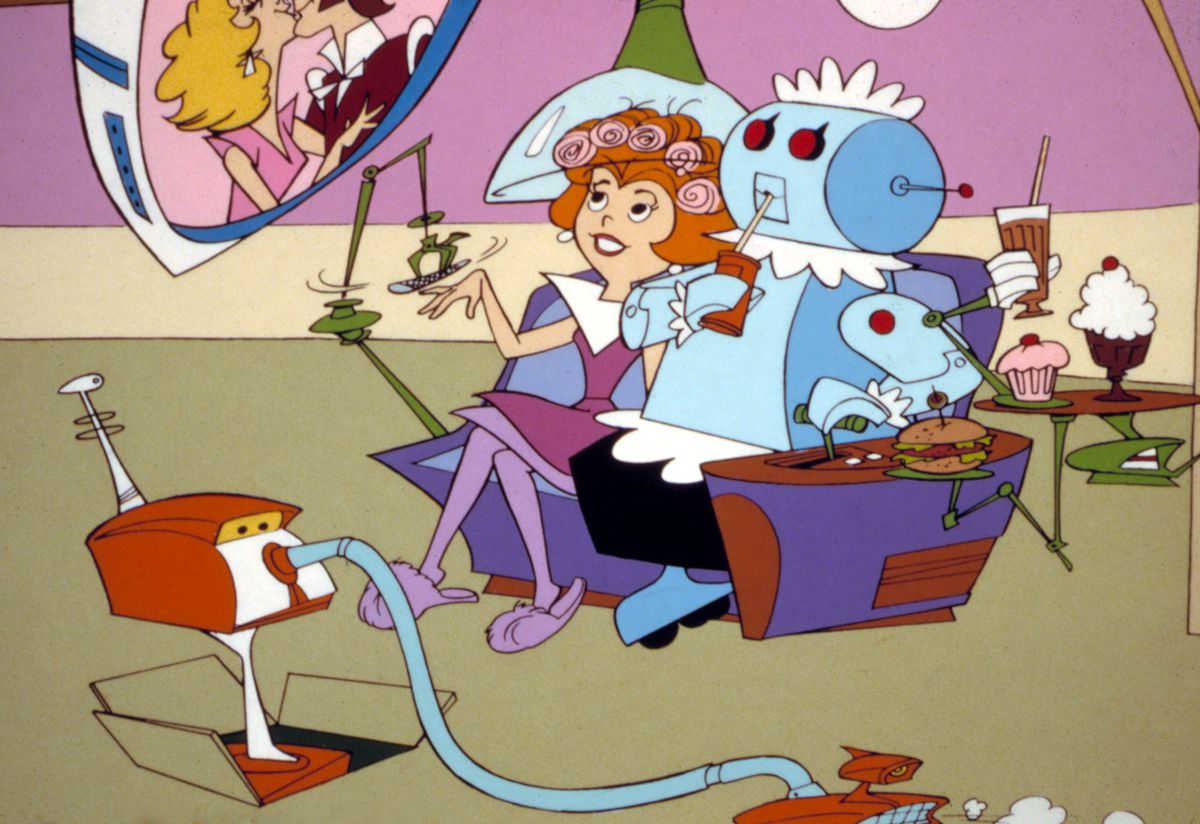 A cartoon scene from the TV show The Jetsons. A robot maid sits next to Jane Jetson on a purple couch. Jane is getting her hair and nails done by robotic machines. The robot and Jane are watching a video screen.