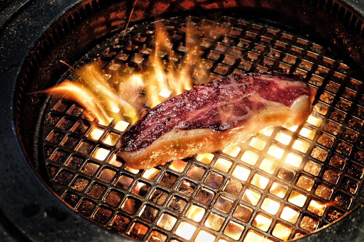 A steak engulfed in flames on a grill.