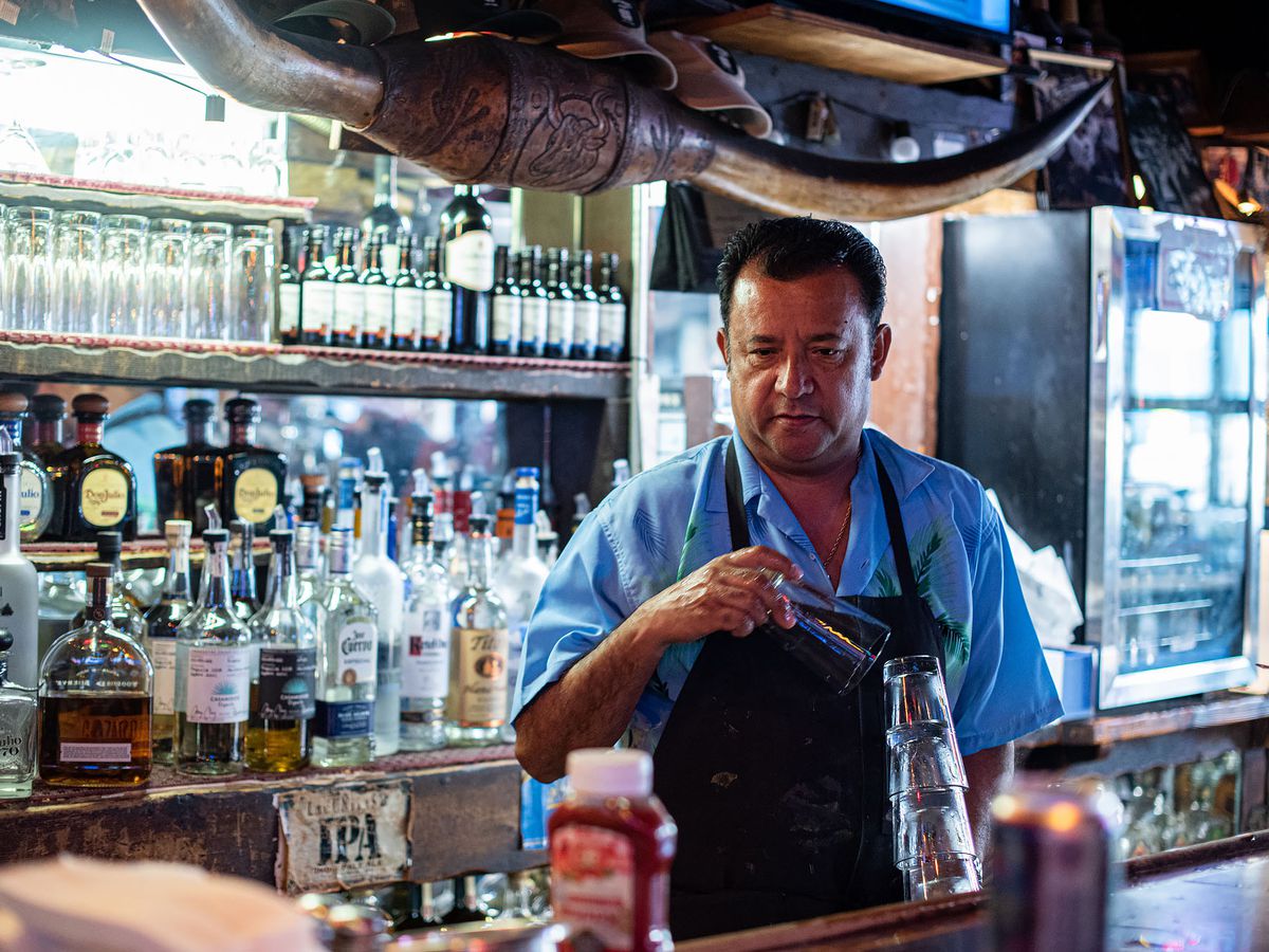 A blue shirted cook at a dive bar, replacing glasses.