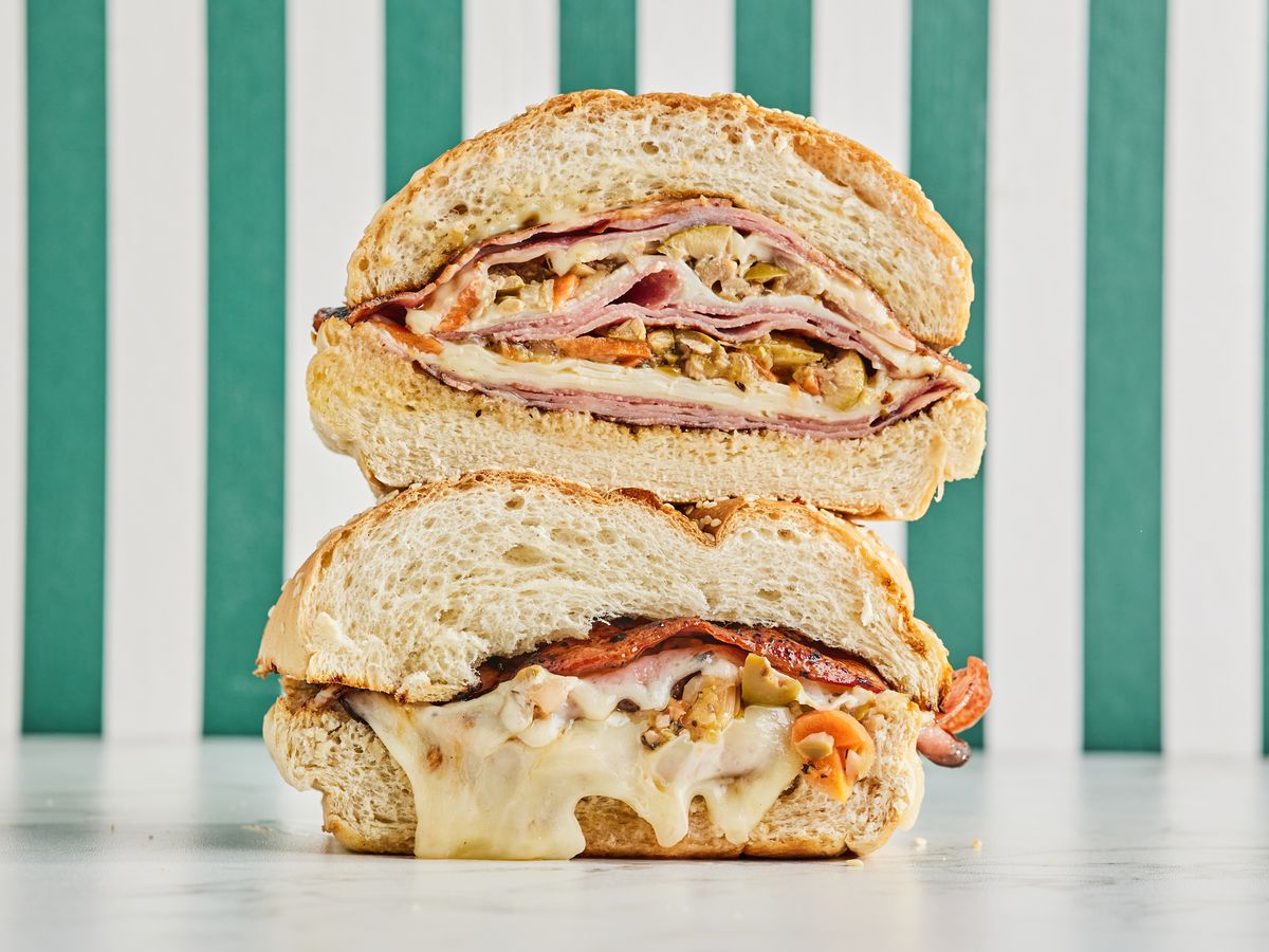 Two sandwich halves stacked in front of a textured background. The bottom sandwich oozes cheese.