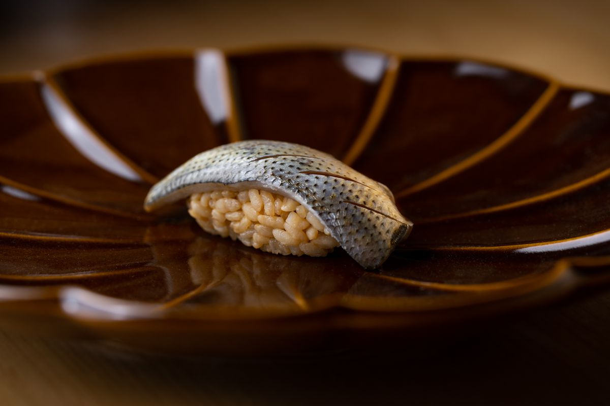 Pickled small fish with knife grooves atop sushi rice.