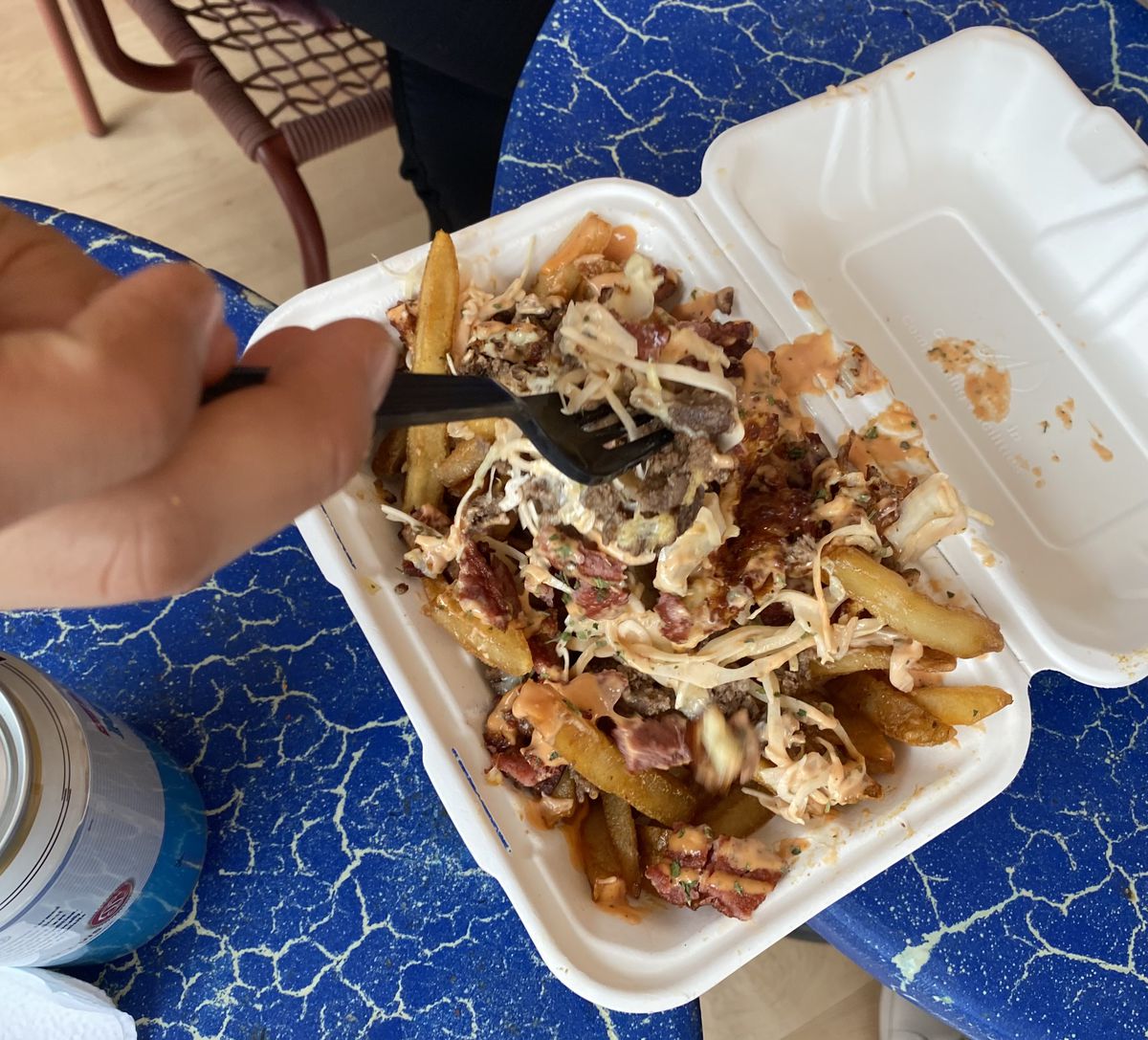 A white takeout container is loaded with crisp french fries topped with chopped cheese and salami.