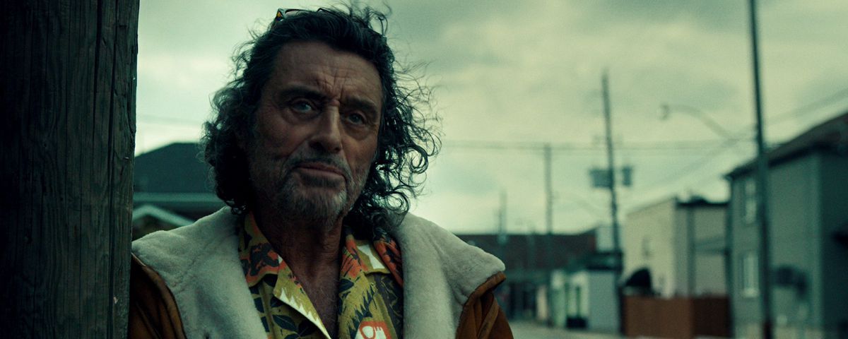 A battered-looking Ian McShane leans against a wall in American Gods