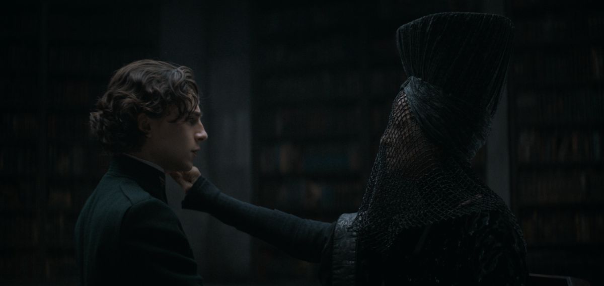 Reverend Mother Mohiam (Charlotte Rampling) touches Paul (Timothée Chalamet) on the cheek in a dark room in Dune