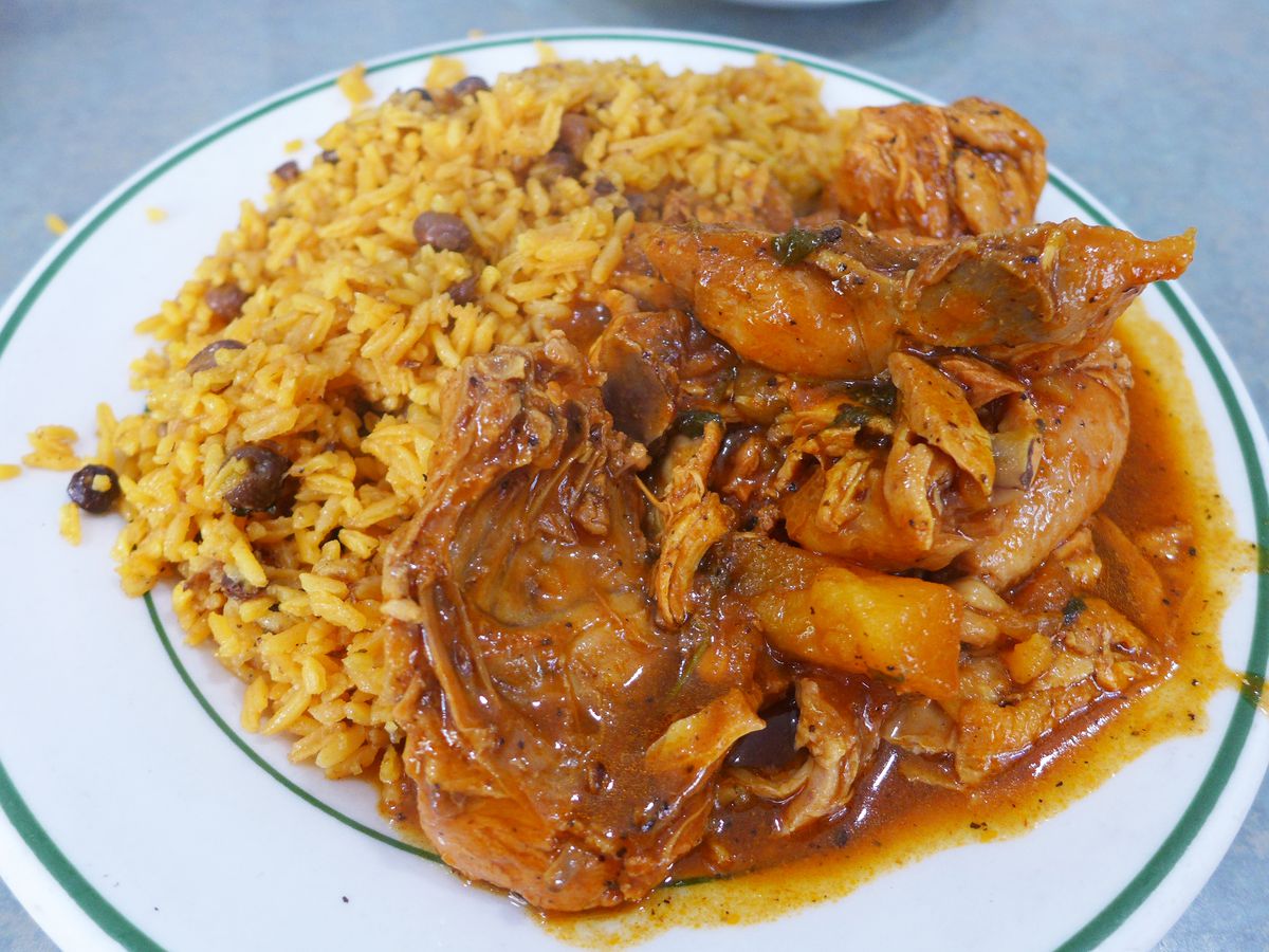 A pile of yellow rice and peas with a juicy chicken stew next to it.