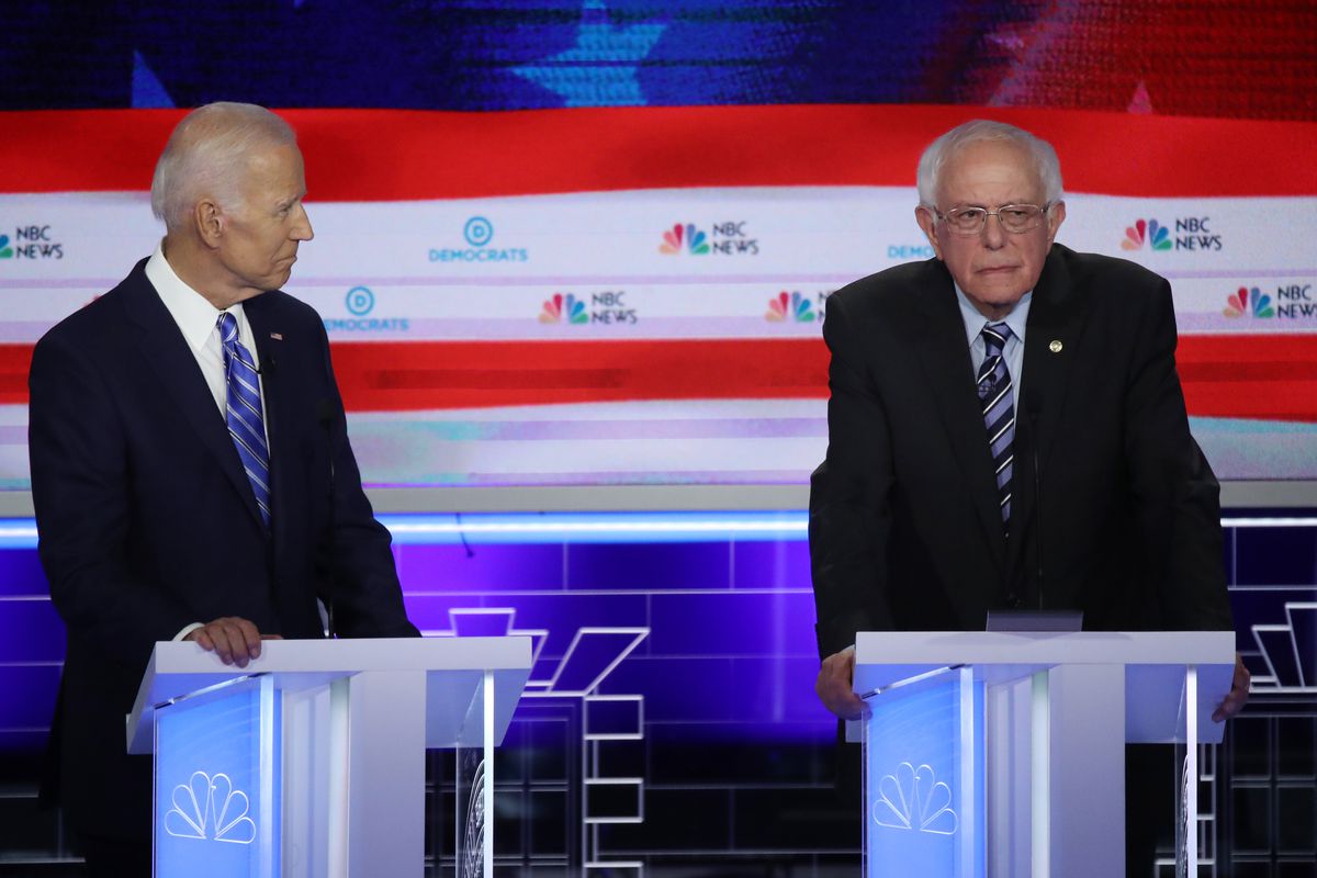 Former Vice President Joe Biden and Senator Bernie Sanders stand behind podiums onstage at the first Democratic debate of 2019.