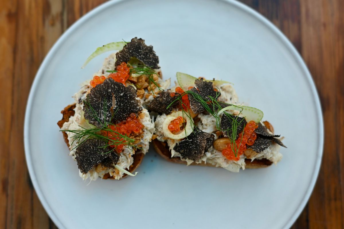 A plate of two slices of toast topped with crab, red fish eggs, and black truffles.