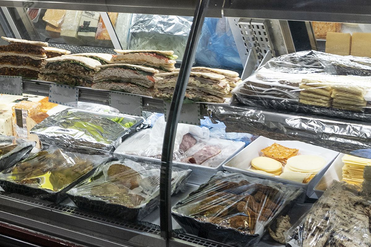 A bodega counter is stocked with beef patties, deli meats, sandwiches, and more.