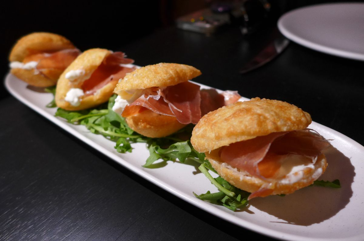 Four little sandwiches rest on arugula on a narrow plate.