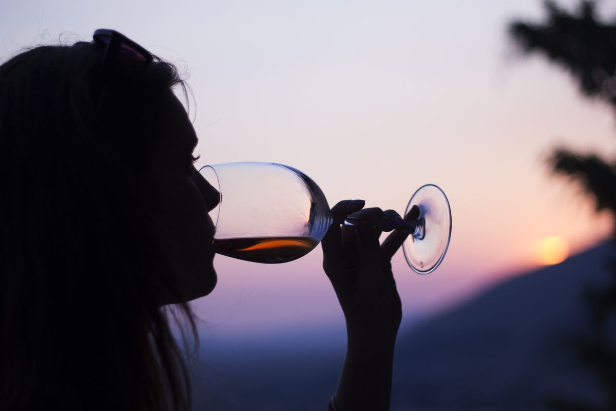 The silhouette of a woman as she drinks red wine outside at sunset.