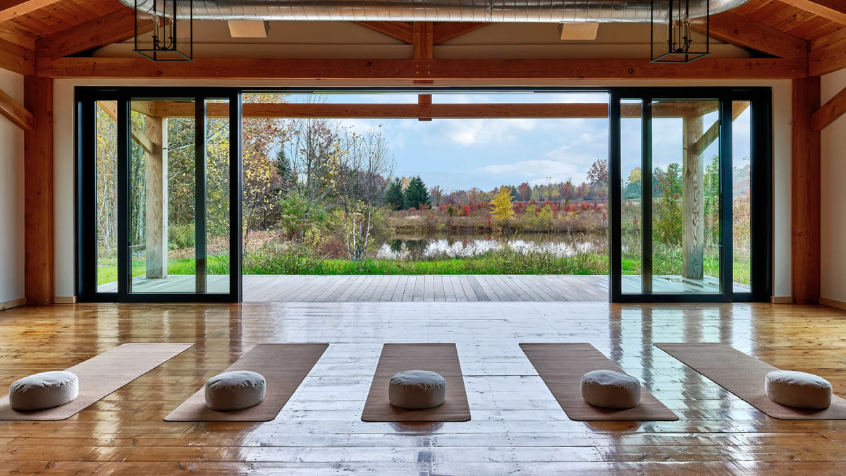 Yoga mats laid out on a wide wood floor in a tall wood structure with a large open wall to the outdoors. 