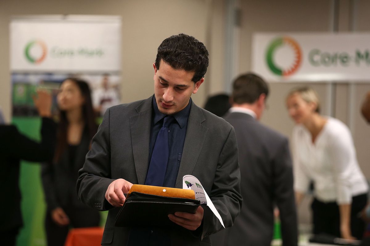 A young man looks at papers in his hand while he walks through a job fair