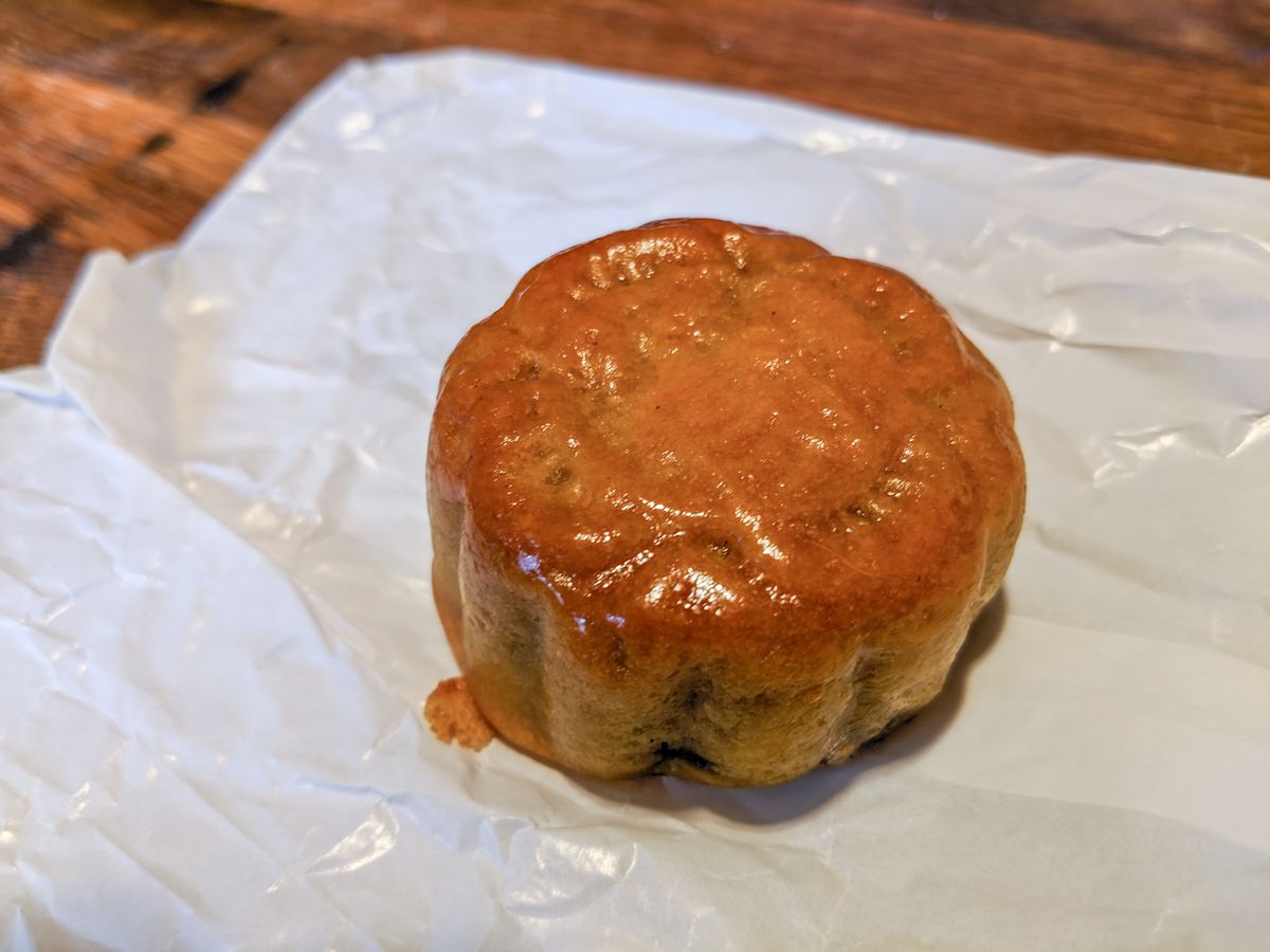 A small red bean mooncake with a glossy pastry shell sits on a white paper bag on a wooden table