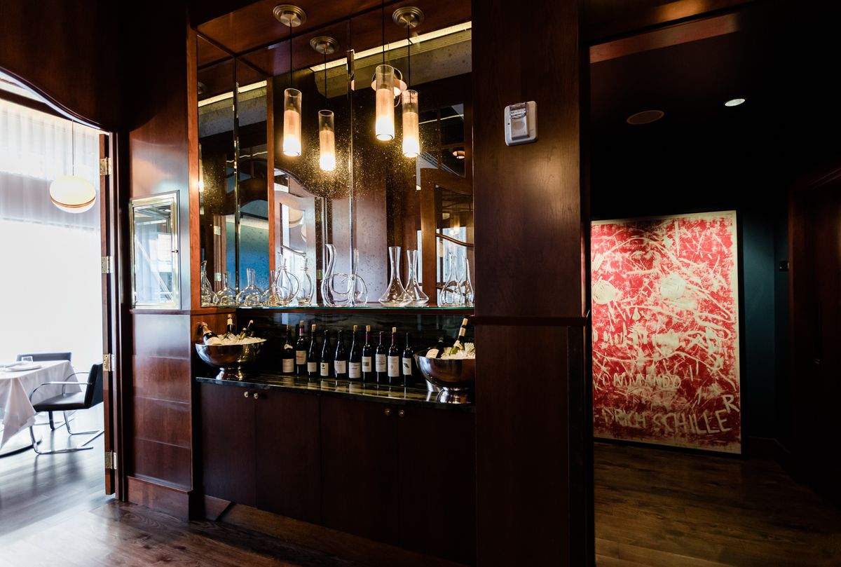 The bar is shown in a dark nook with mirrors, wine bottles, and glass decanters.