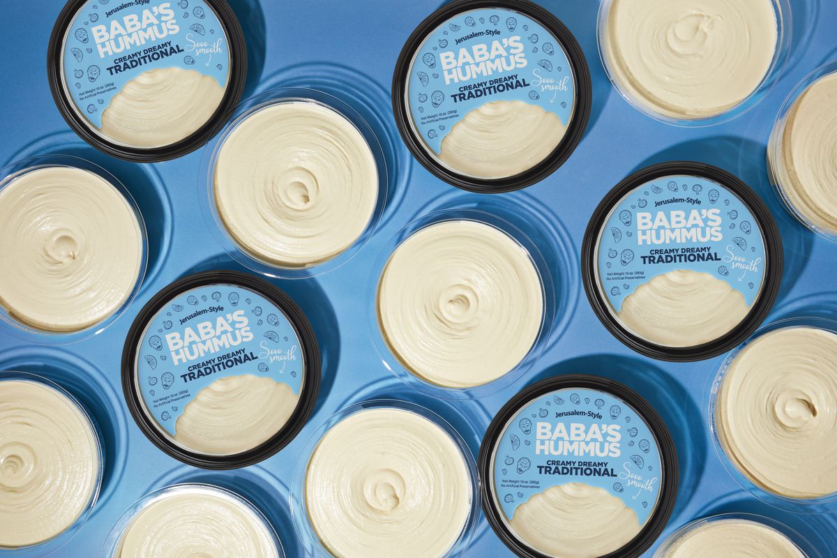 An assortment of round tubs of hummus with blue labels against a blue background. 