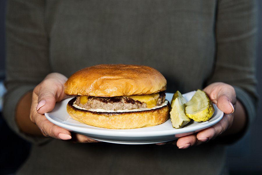 Everson Royce&nbsp;Bar’s burger, a thick single patty on a low, wide bun, held on a plate in the air with two hands.