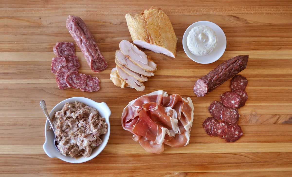 Sliced meats and dips arranged on a wooden board