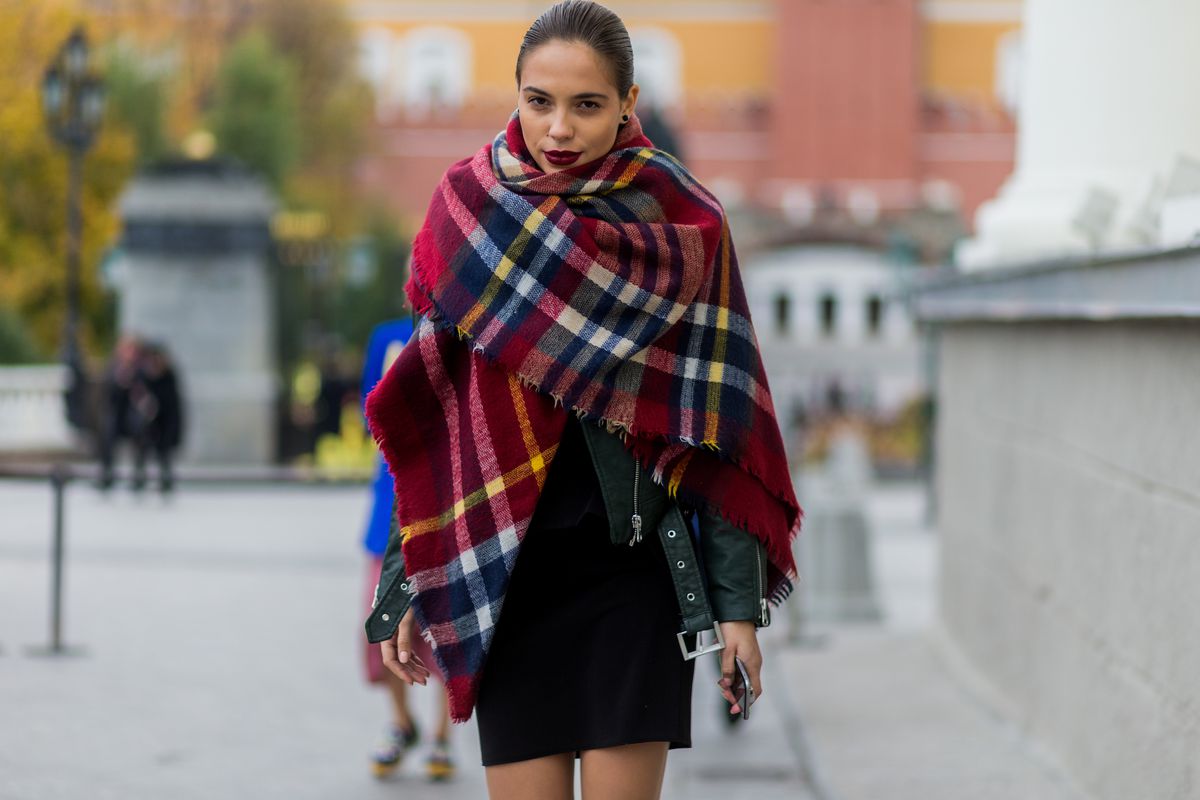 Woman walks down street in blanket scarf.
