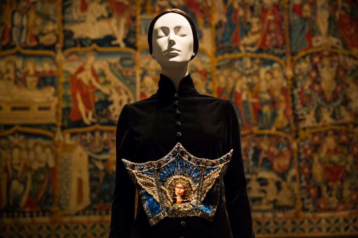 A mannequin wears a long black robe with an embroidered icon on the chest.