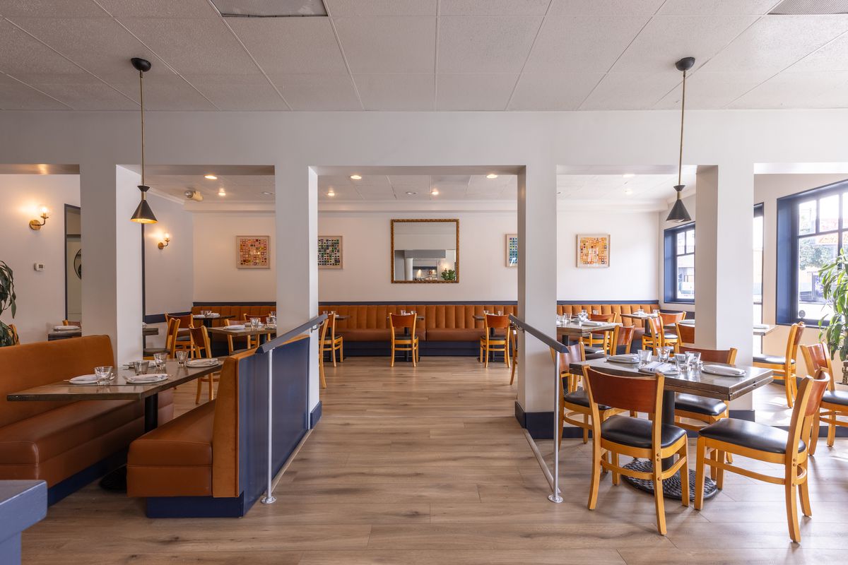 Een zonnige eetkamer met houten vloer, diepblauwe accenten en hoge pilaren in het midden, in het nieuwe Vicini in Los Angeles.