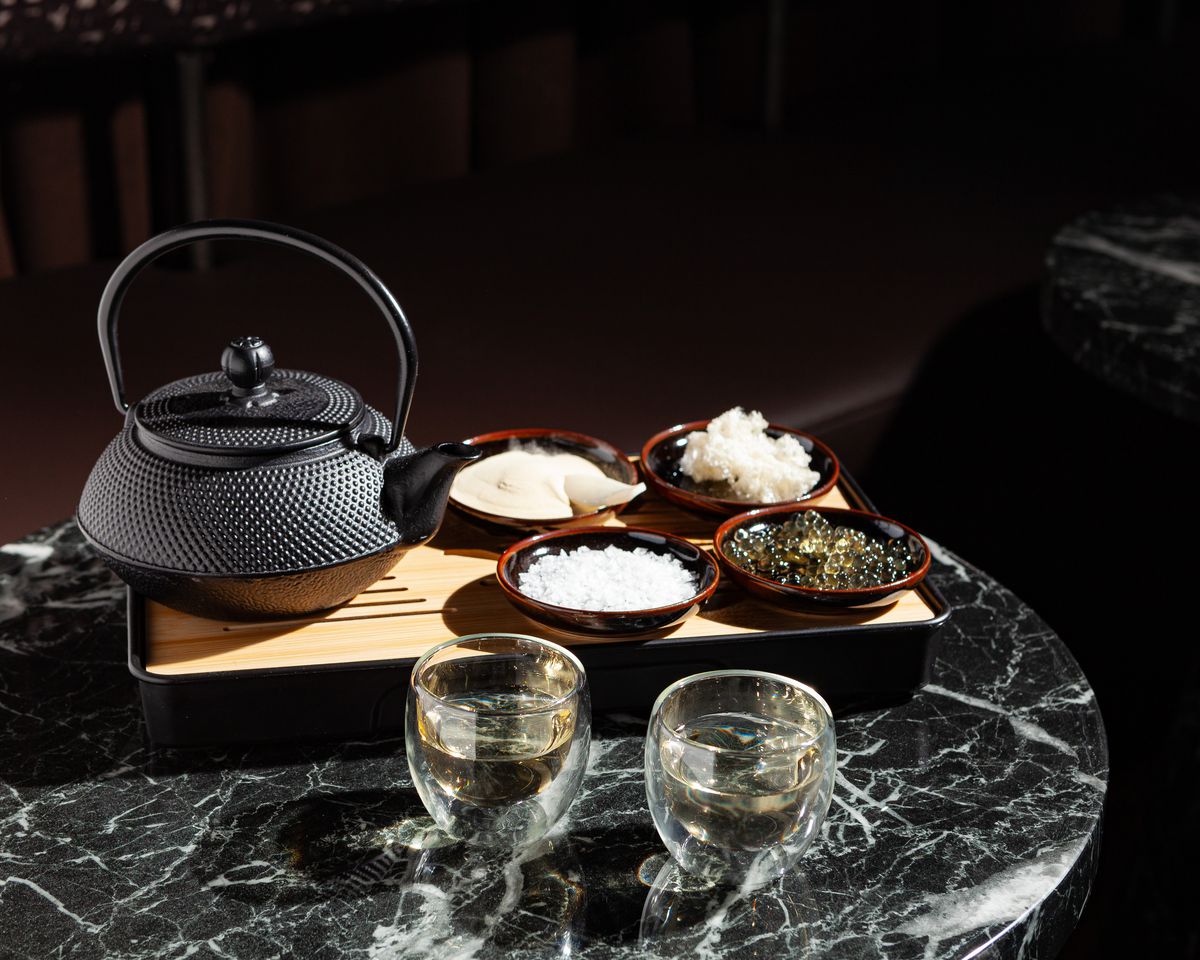 A cast iron teapot sits beside four small plates of honey and two small glass sake cups.