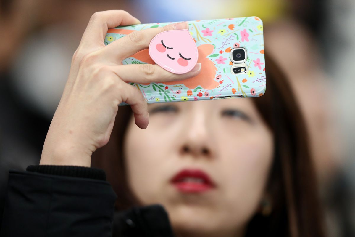 A young woman holds up her phone to take a picture.