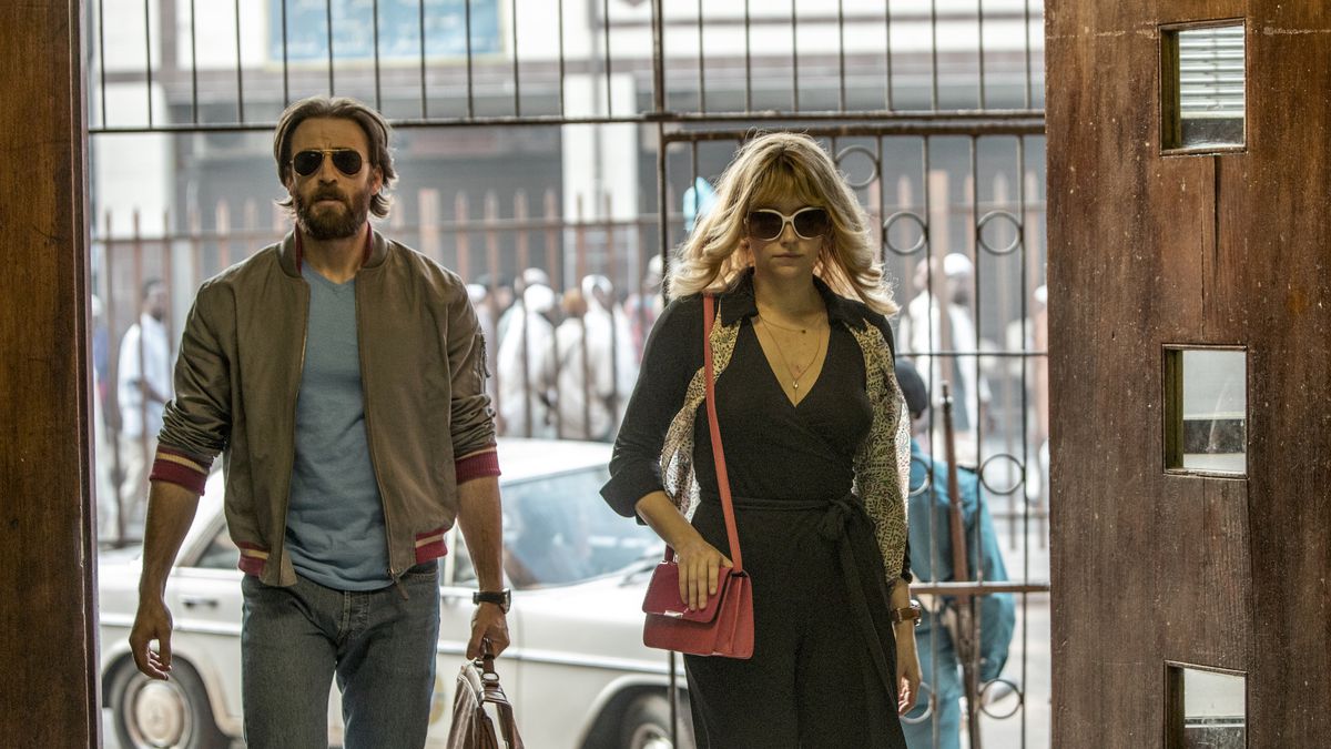Carrying their luggage, Ari Levinson (Chris Evans) and Rachel Reiter (Haley Bennett) walk into a lobby in The Red Sea Diving Resort