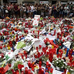 People stand next to candles and flowers placed on the ground after a terror attack that killed 14 people and wounded over 120 in Barcelona, Spain, Sunday, Aug. 20, 2017. (AP Photo/Manu Fernandez)