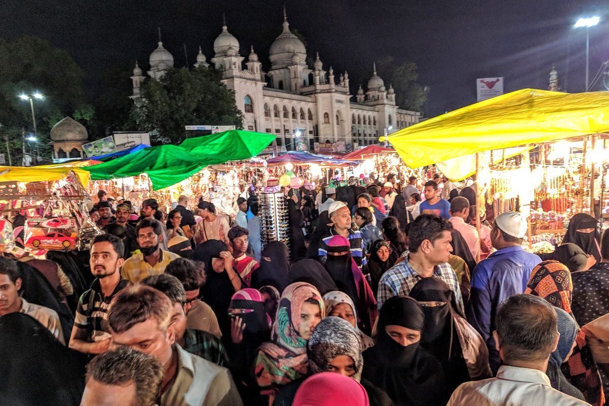 A crowd among stalls topped with colorful umbrellas at night.