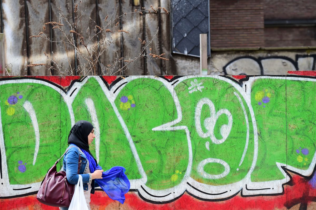 A Muslim women wearing a hijab walks past a graffiti near the European institutions in Brussels, June 15, 2015.