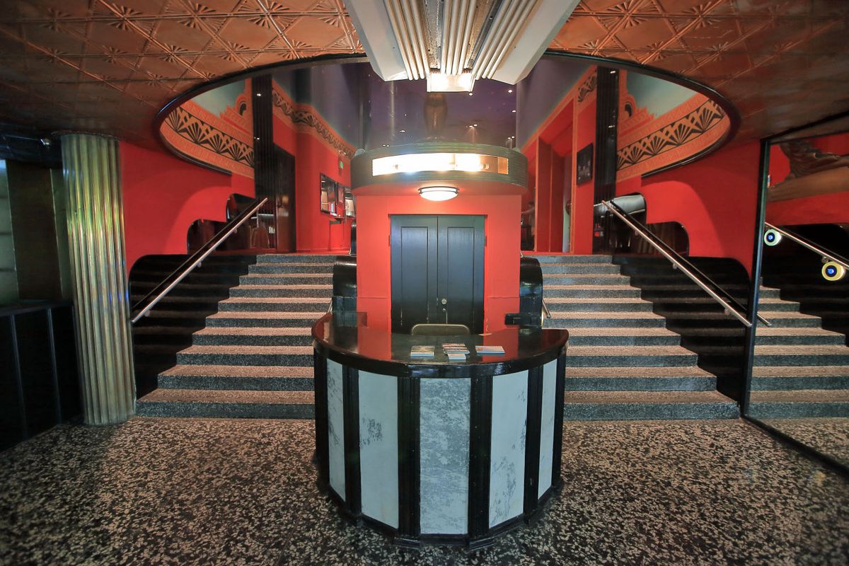 A ticket desk at the foot of a dramatic staircase, under a cut-out in the ceiling that is a circle that opens to the stairs. 