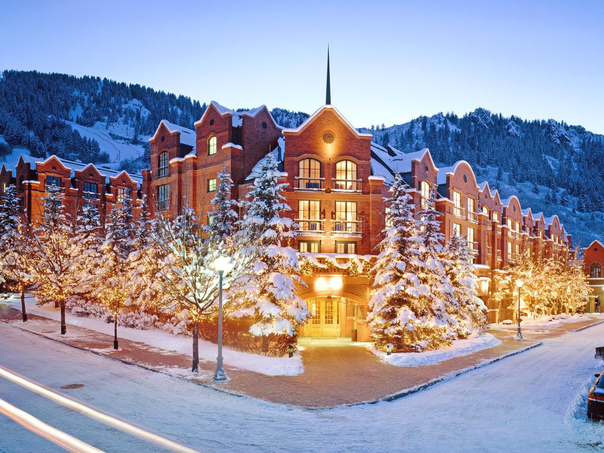 A view of a red brick hotel on a corner at twilight, with the building covered in snow. Trees are wrapped in white lights and planted on either side of the building.