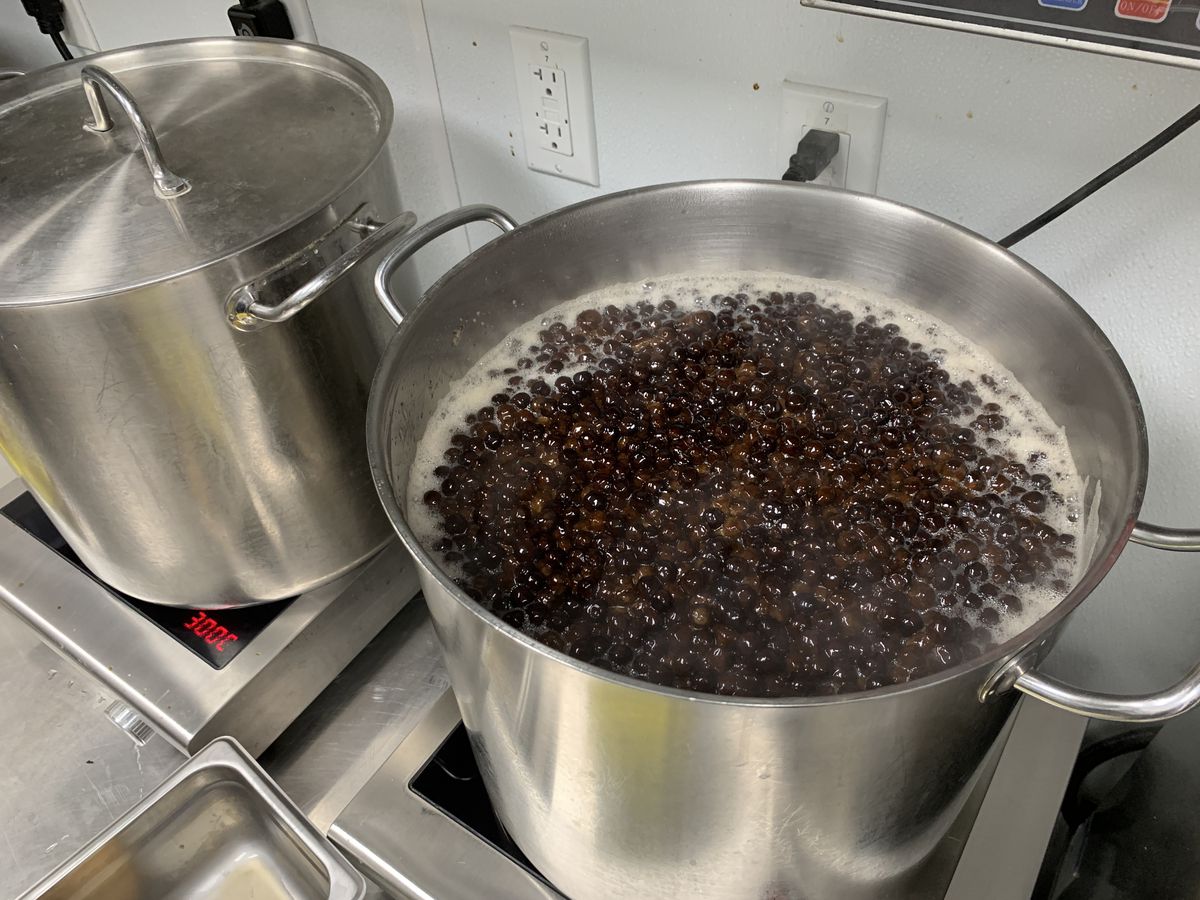 A pot of boba boils in a stainless steel pot on a stove.