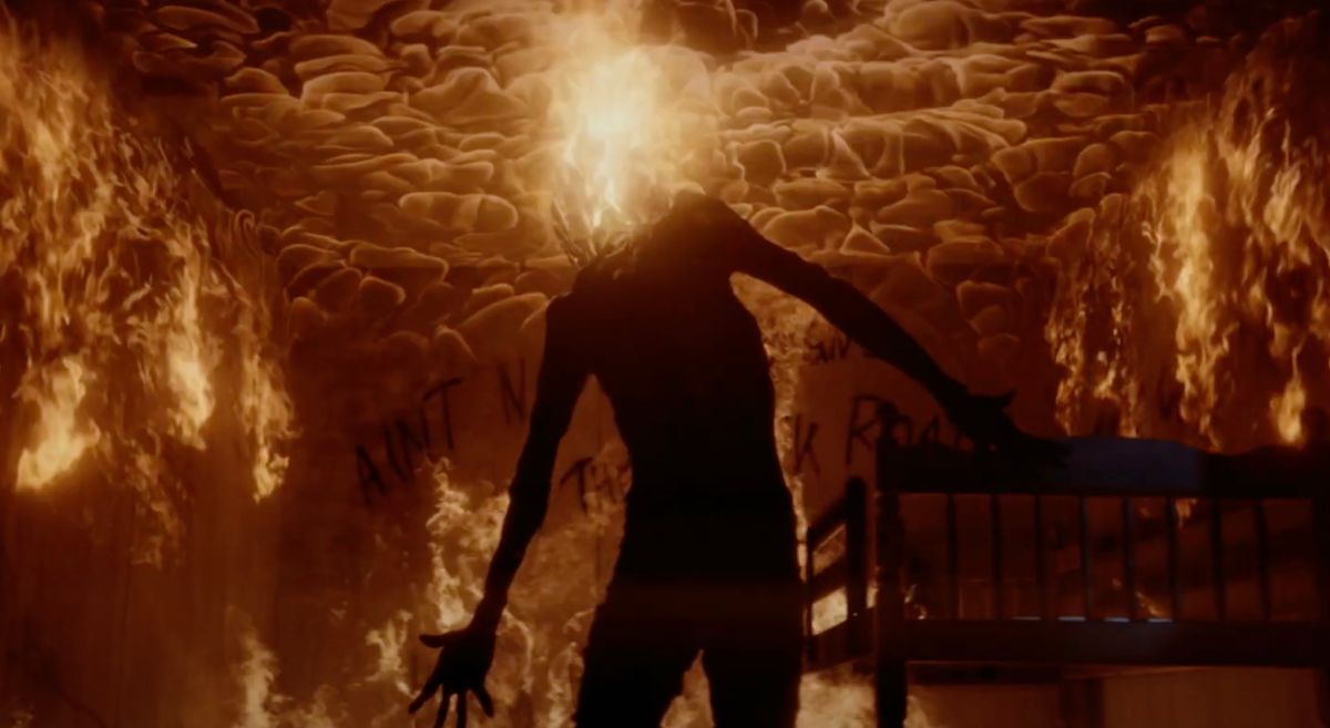 A headless figure stands in a room engulfed in flames, a plume of fire spewing out of their neck in Dark Harvest.
