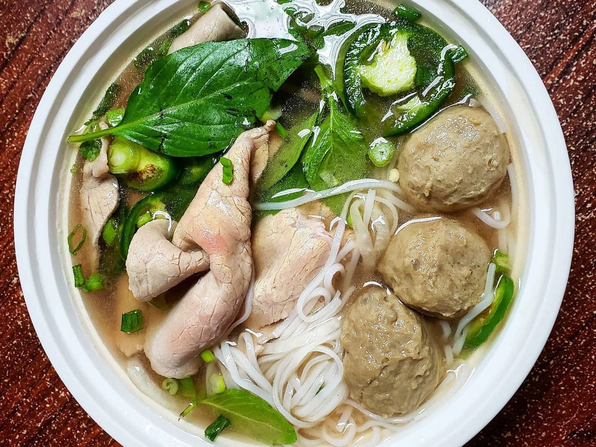 An overhead shot of a bowl of Pho Tai Bo Vien Pho with Rare Steak and beef balls, basil, noodles, and jalapenos